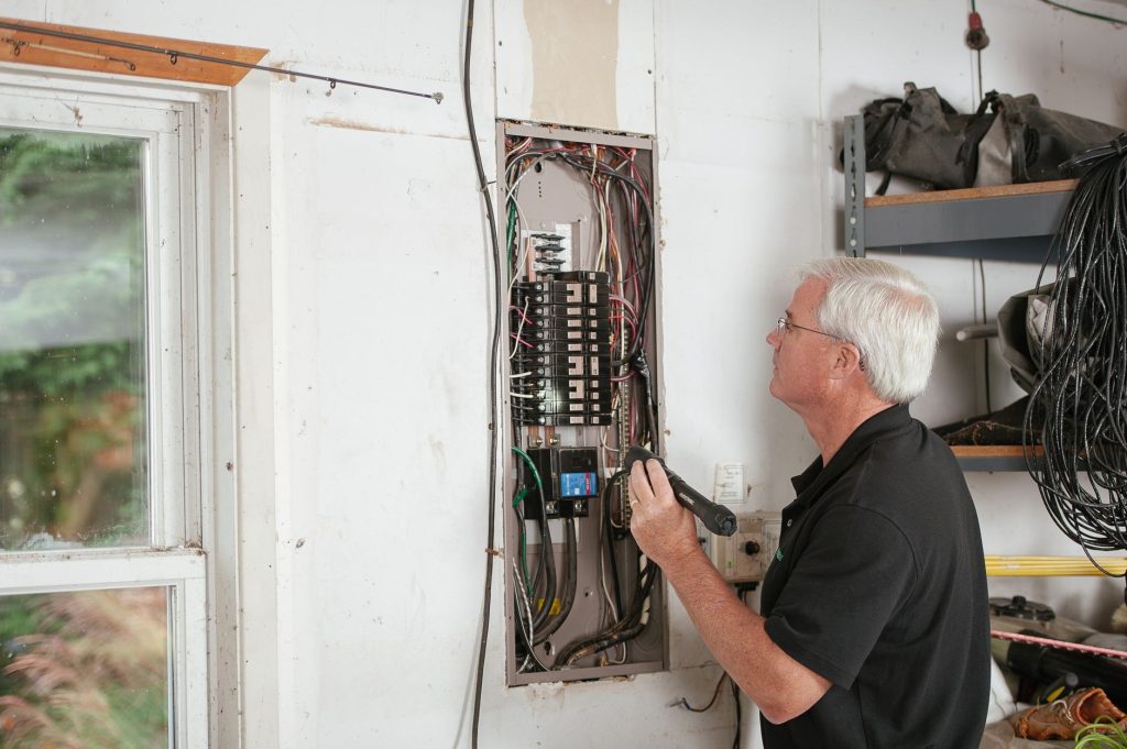 Technician using a flashlight to inspect an open residential electrical panel